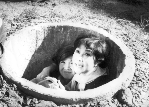 Black and white still of two children in a well.